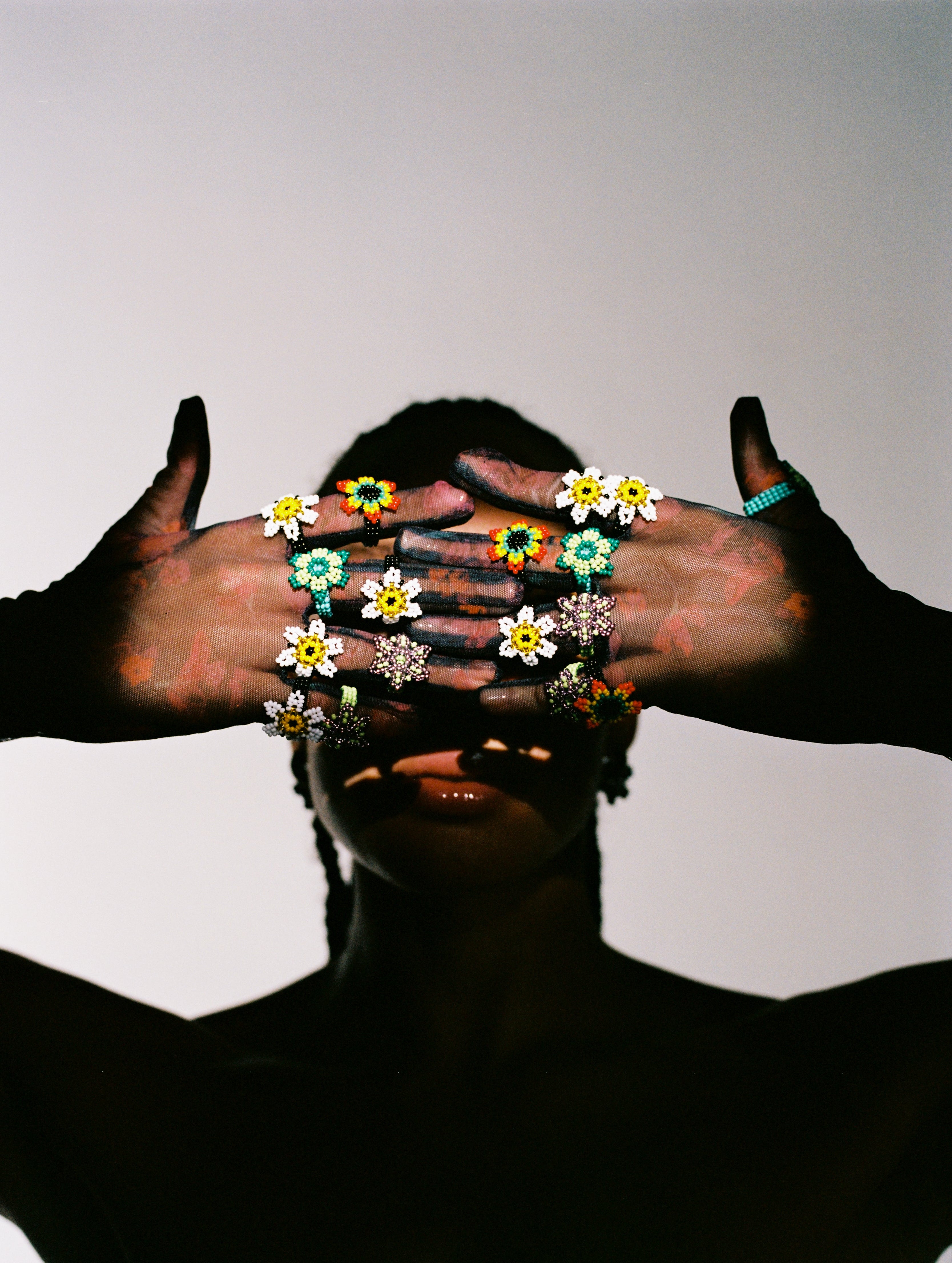 Person with floral rings on fingers against a neutral background